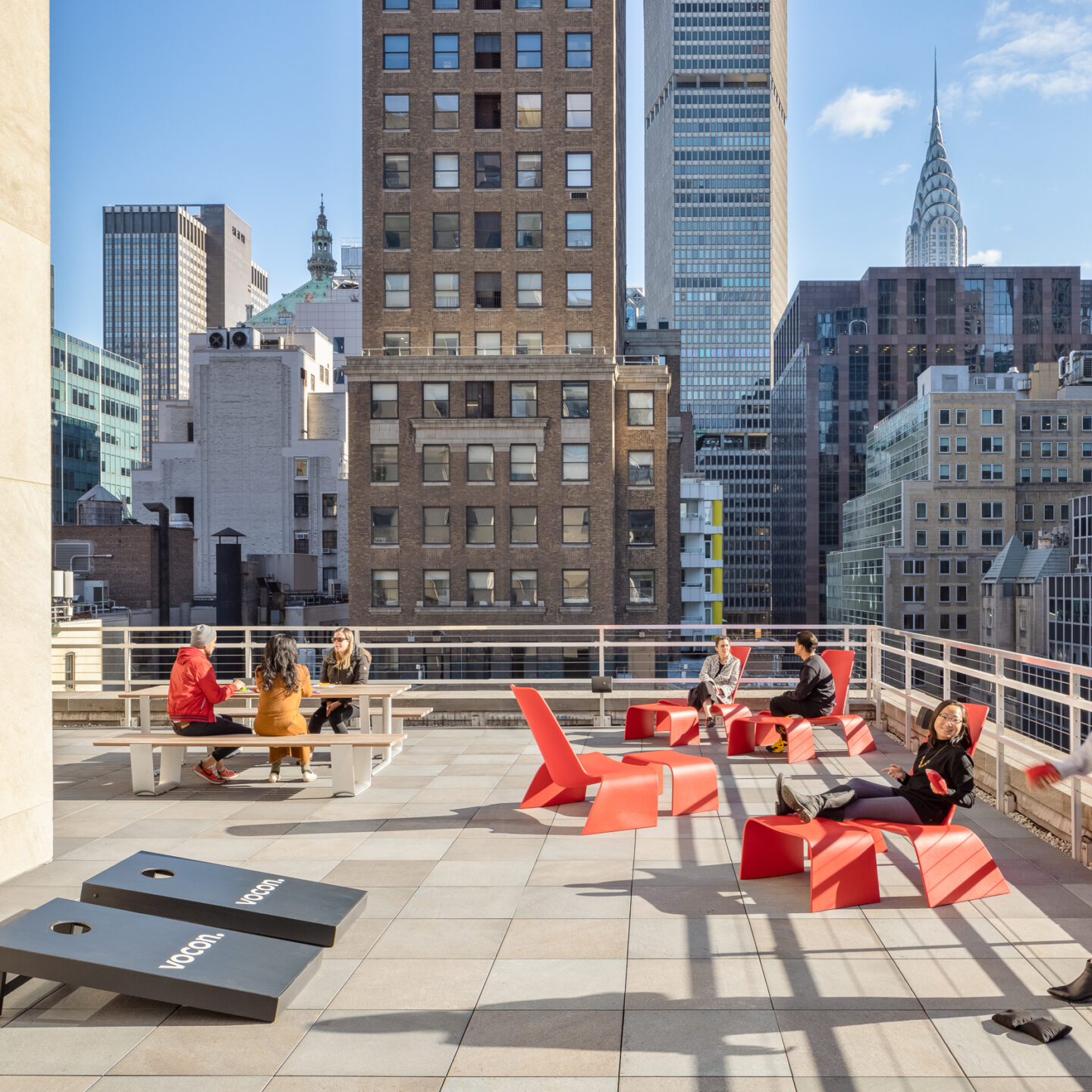 People play cornhole and socialize on a New York City terrace on a sunny day.